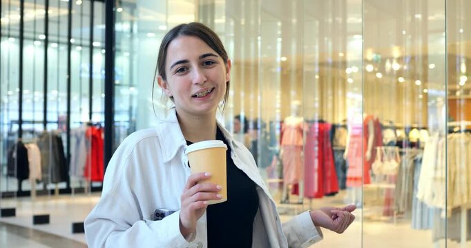 Woman sipping coffee outside boutique glass storefront, holding cup, casual jacket, shopping bags in background, warm golden lights, reflective displays, thoughtful smile, relaxed shopper vibe