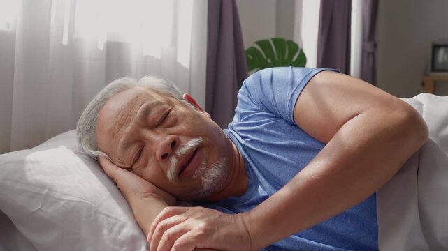 Elderly Asian man sleeping peacefully on bed in cozy bedroom with natural sunlight morning light. Hhealthcare retirement concept	