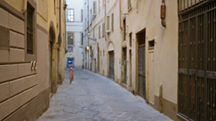 Obraz premium Narrow european cobblestone alley out of focus with shallow soft bokeh, muted beige facades and empty pavement; background copyspace backplate calm.