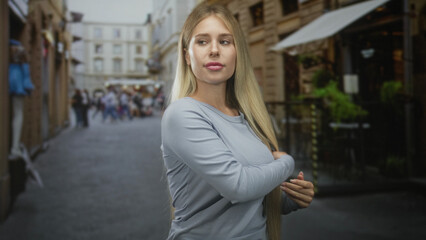 Fototapeta premium Woman touching long hair on a narrow street, adjusting her sweater and gazing sideways at storefronts; poised confidence.