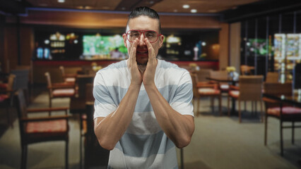 Obraz premium Man with red glasses and striped shirt pressing hands to face, rubbing eyes and nose in a dim restaurant dining area inside a building; fatigue.