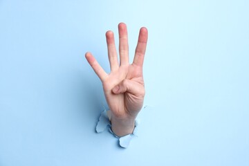 Naklejka premium Woman showing number four with fingers through hole in light blue paper, closeup
