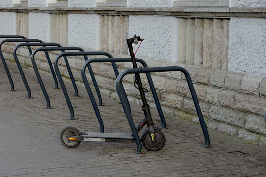 Electric kick scooter parked and locked near bicycle rack on city street against stone building wall in urban environment. Modern eco friendly transportation and micromobility concept in Europe.
