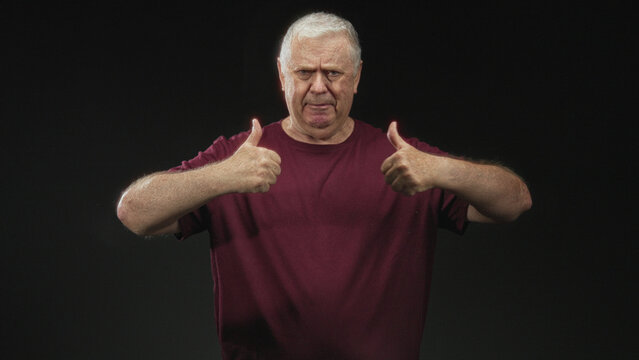 Man gives double thumbs up with visible thumbs and forearms in studio wearing burgundy tshirt amid varied facial expressions; hesitation humor.