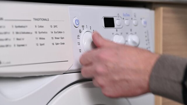 A man's hand sets the automatic washing program switch on the washing machine panel. Saving water and natural resources.