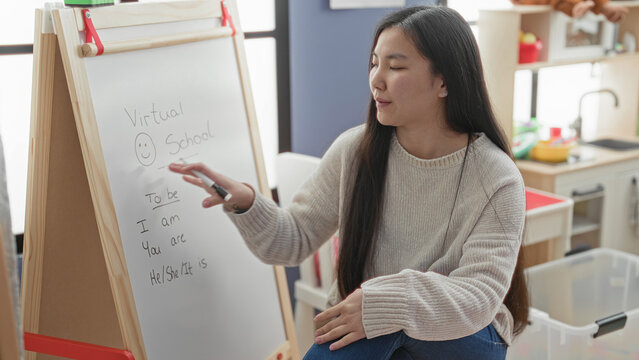 Woman teacher gestures with marker at whiteboard in studio, pointing hand visible while explaining present tense verbs to camera; engaged learning connection.