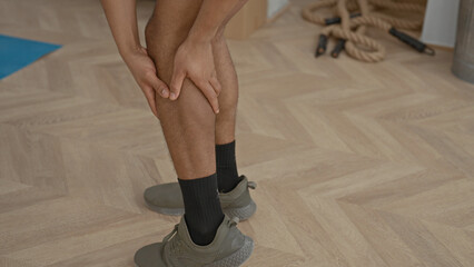 Man holding calf and massaging lower leg beside exercise mat and battle ropes in studio  recovery training. © Krakenimages.com