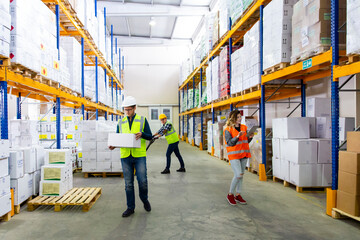Fototapeta premium Three workers, two men and one woman, are shown in a warehouse setting, wearing safety gear and handling materials. depicts an industrial environment with shelving units stocked with boxes and pallets