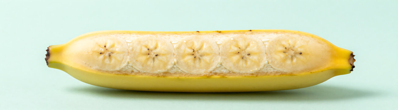 lengthwise halved banana lies soft pastel mint background illuminated gentle overhead natural light emphasizing