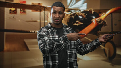Man holding screwdriver pointing finger in building with biplane exhibit and wooden propeller visible, gesturing repair work  instructional confidence. © Krakenimages.com
