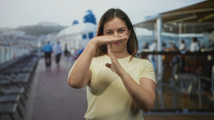 Fototapeta premium Young woman with hands making time out gesture on sunny cruise ship deck near railing; calm pause reflection.