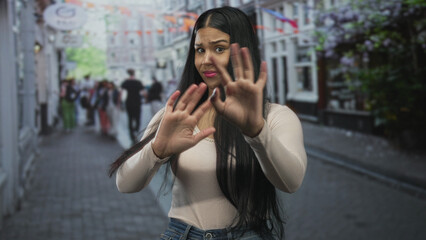 Fototapeta premium Latin woman pinches nose on bustling city street in front of storefronts to block foul odor; disgust.