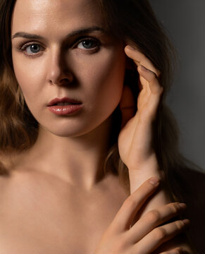 Woman's portrait with bare shoulders, hands gently touching her face and neck