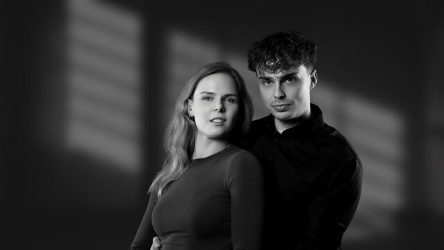 Young couple posing together in a studio setting with window shadow