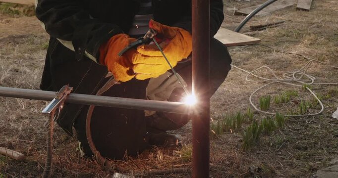 Professional welder joining metal pipes with an electrode welding machine, creating bright sparks and smoke during the steel fabrication process, then taking off his protective mask.