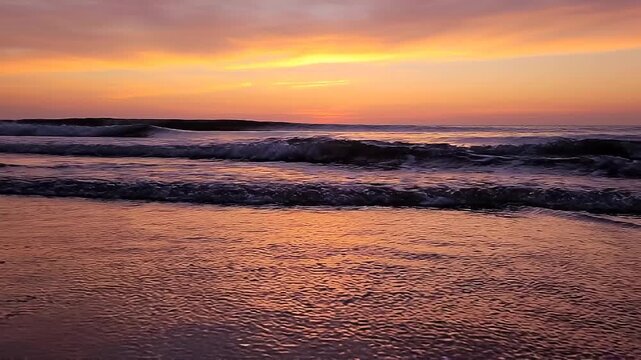 Dramatic beach sunset with vibrant orange and yellow clouds reflected in the wet sand and gentle ocean waves creating a colorful and atmospheric seascape Keywords: sunset, beach, ocean, sea, waves