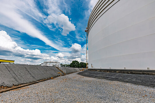 White storage fuel tanks group with oil pipeline system in petrol industry area at harbor against blue clound sky .