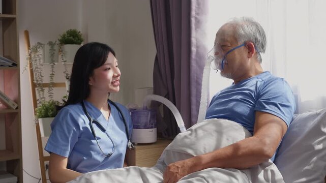 Professional Asian woman caregiver supporting elderly patient man with nebulizer mask breathing treatment oxygen therapy on bed at home. Healthcare Assistance concept.
