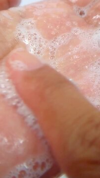 Close up of rubbing white foam on palm of hand using index finger. Detailed view of foamy texture and gentle spreading motion on clean white background.