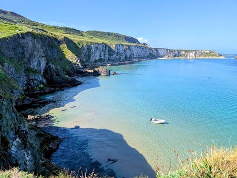 Aerial view of Kinbane Head and turquoise bay with a small boat, white cliffs and lush green hills on the North Antrim Coast, Northern Ireland.