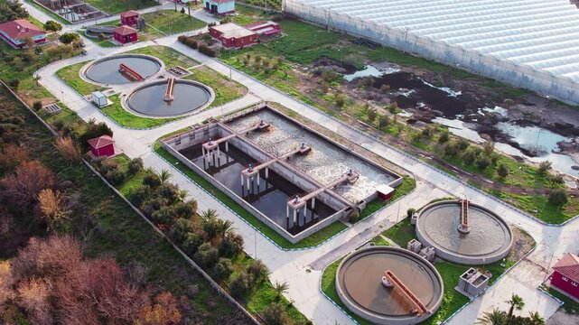 Drone aerial view of modern wastewater treatment plant with circular clarifier tanks, rectangular aeration basins and organized service roads