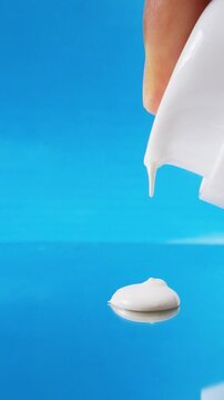 White beauty cream dripping onto reflective glass surface with blue background. Close up texture, cosmetic product concept for skincare.