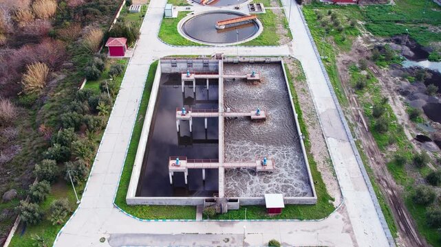 Aerial view of wastewater treatment facility featuring large circular clarifier tanks and rectangular processing basins arranged in symmetrical layout. Water purification and environmental management