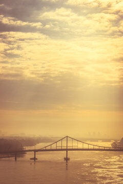 Bridge over the river in golden hour. Dramatic evening sky with cityscape and bridge. Spring Kyiv landmark, Ukraine. Sunrise above Dnipro river. Transportation bridge over the water. Big city in dawn 