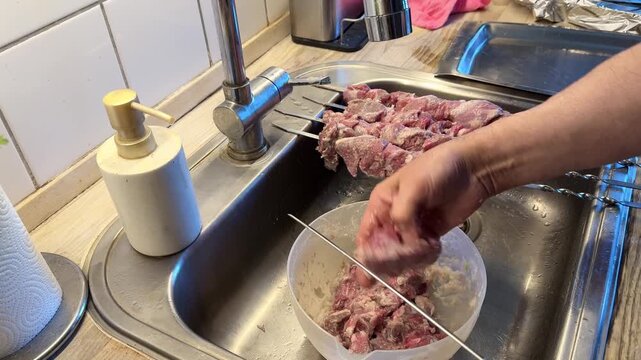 Man Threading Marinated Lamb Meat onto Skewers for Barbecue.