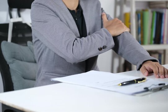 Feeling pain in the elbow and arm while sitting in front of the laptop in the office environment. The tired man massaged his arm muscles with a painful expression on his face indoors, exhausted after 