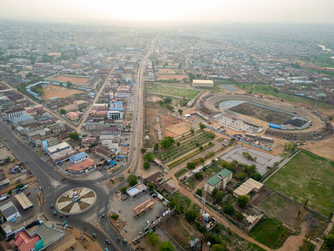 Kaduna, Nigeria - 13 May 2026: Aerial view of the Ahmadu Bello Stadium under renovation surrounded by urban sprawl, a busy roundabout, and residential buildings under a hazy sky.