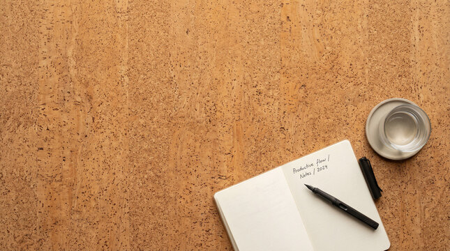 Top view of open notebook with pen and water glass on cork background