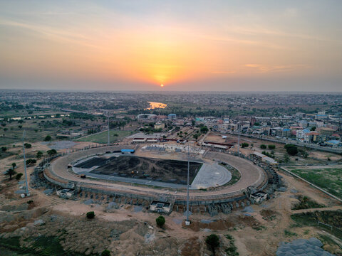 Kaduna, Nigeria - 02 May 2026: Aerial view of Ahmadu Bello Stadium showing the running track and field under renovation against the backdrop of the city skyline at sunset.