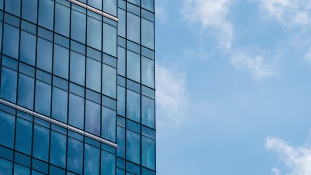Close up timelapse of skyscraper glass facade reflecting moving white clouds, blue sky mirrored in windows, modern architecture texture and urban design concept