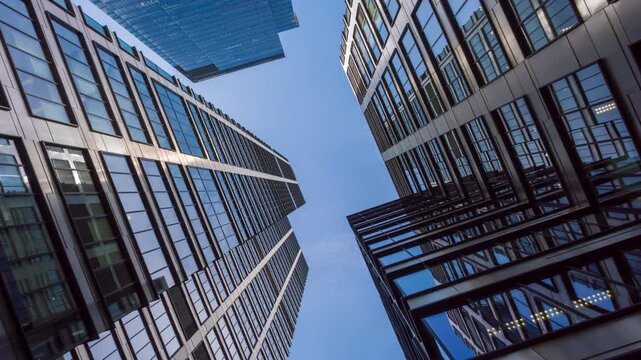 Low angle wide shot time-lapse of downtown high-rise glass skyscrapers on sunny day, financial district looking up tall modern architecture office buildings city center street, blue sky white clouds