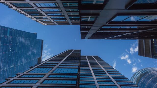 Low angle hyperlapse motion time-lapse downtown high-rise glass skyscrapers on sunny day, financial district looking up tall modern architecture office buildings city street, blue sky white clouds