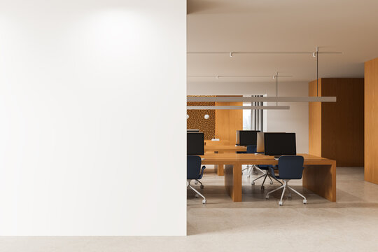 Modern office interior featuring a large blank wall for poster mockup beside an open workspace with wooden desks and minimalist design elements. 3D Rendering
