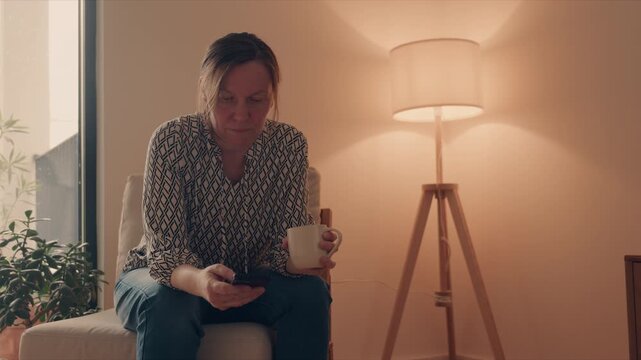 Mature woman checking smartphone with cup of coffee indoors, cozy communication and everyday routine concept, 4K