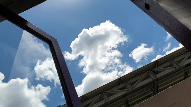 A perfectly open wooden window frame reveals a majestic towering white cloud formation centered against a vivid blue sky, glowing beautifully beside a long metallic canopy structur