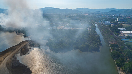 Fototapeta premium Aerial view of a landfill fire in Phuket with heavy smoke spreading across nearby landscapes and urban areas. Thick plumes of smoke rise illustrating the impact of urban waste and air pollution.