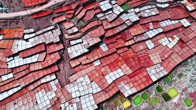 Red salt evaporation ponds beside a mountain river in a dramatic valley