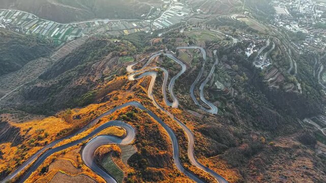 Aerial view of winding mountain road through golden hills and terraced fields