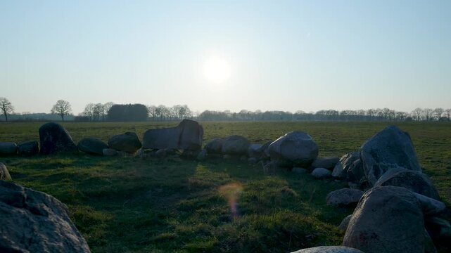 Megalithic burial mound surrounded by stones in a field at sunrise