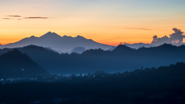 Sunrise over Bali's icon, volcanic landscape, with the sun turning the sky a depp orange colour, and mist filling the valleys below
