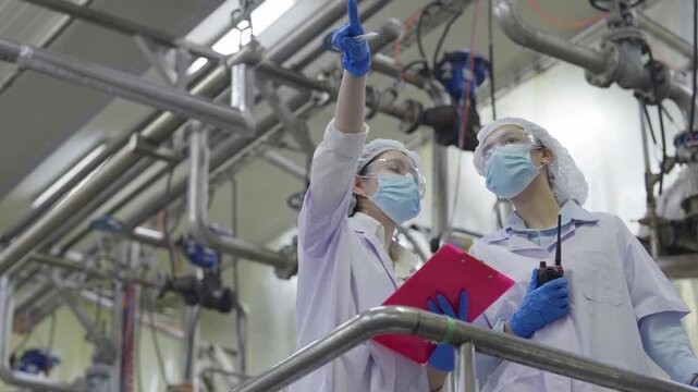 Food factory automated production line, laboratory worker inspecting industrial plant sterile uniform with clipboard and radio, industrial inspection safety glasses and blue glove, clean room