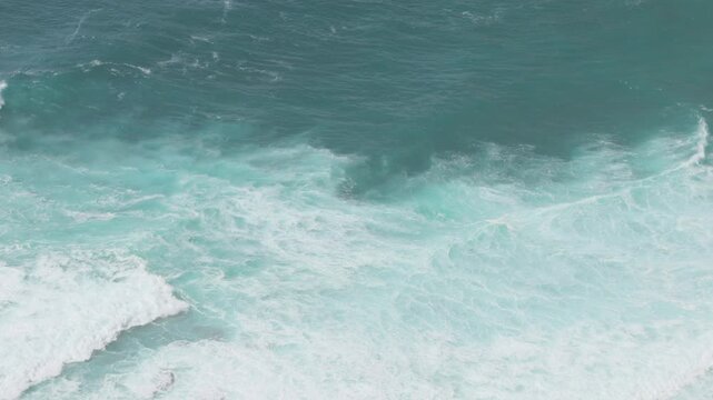 An aerial view of powerful turquoise ocean waves crashing into white foam, showing natural water texture and movement. 4k slow motion stock video