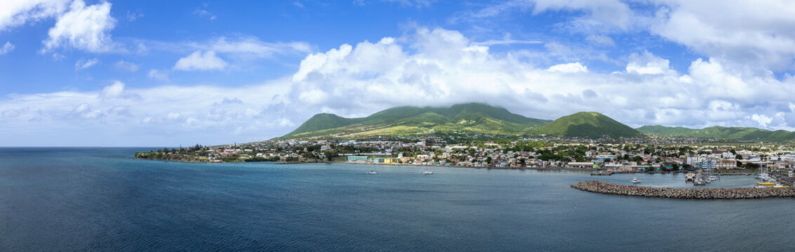Aerial view of the coastal city with its harbor and lush green volcanic mountains under a cloudy sky in Basseterre, Saint George Basseterre, Saint Kitts and Nevis.