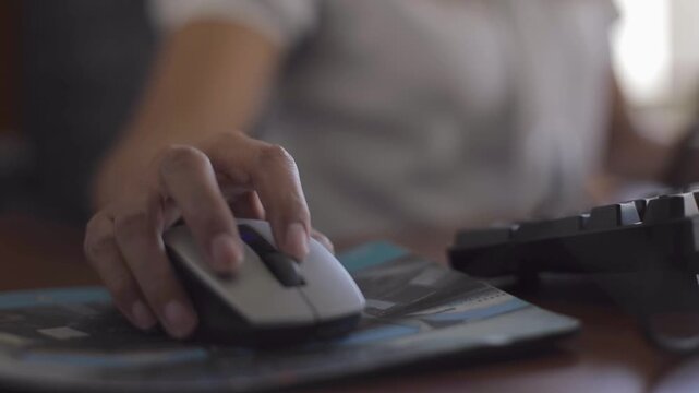 Hand of a dark-skinned woman operating a mouse. On a desk, a woman's hand operates a computer mouse.