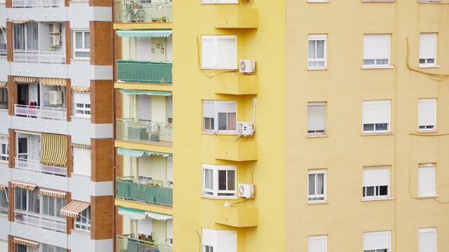 Close-up telephoto view of colorful residential apartment building facades showing yellow and white walls, green-railed balconies, striped awnings, and air conditioning units