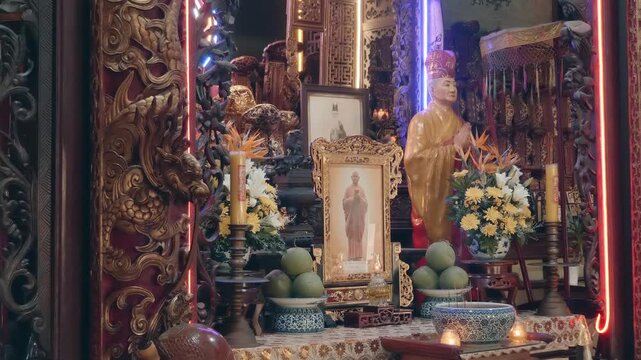 A meticulously decorated altar featuring ornate wooden carvings, a central framed portrait, and a statue dressed in yellow robes inside a temple in Vinh Trang Pagoda in My Tho City in Mekong Delta reg